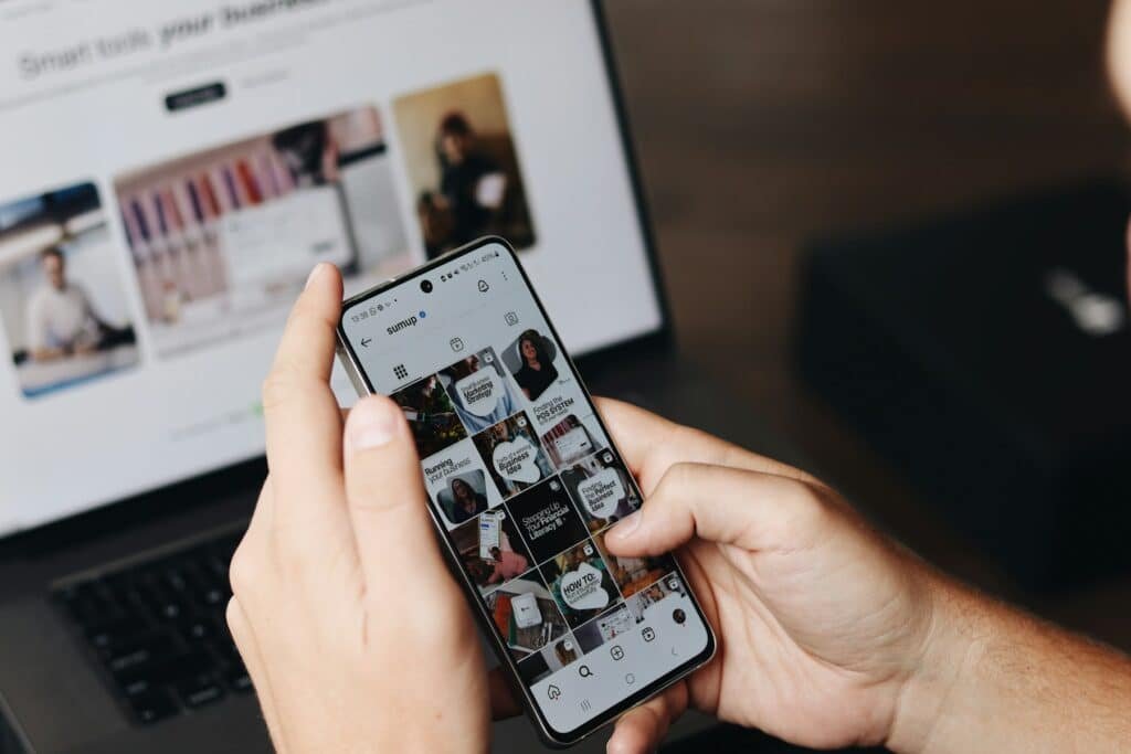 Business owner checking social media on a phone beside a laptop